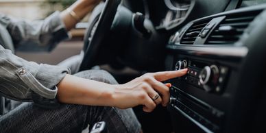 Person adjusting car radio while driving, wearing plaid pants and a striped shirt.